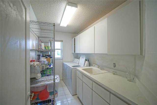 clothes washing area featuring a textured ceiling, light tile patterned floors, sink, washing machine and dryer, and cabinets