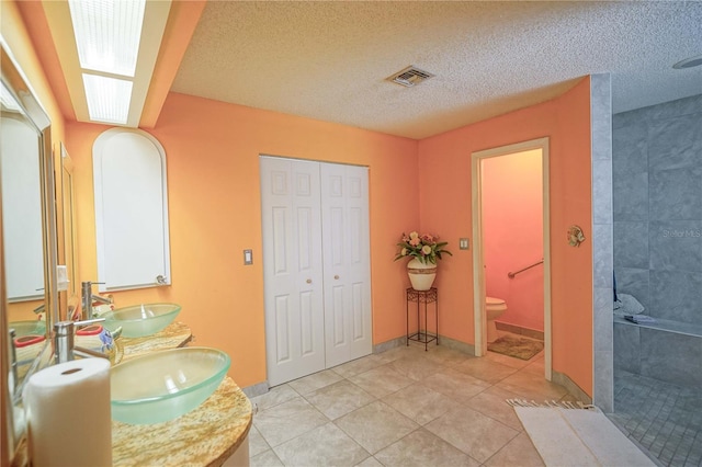 bathroom with a textured ceiling, toilet, a shower, and tile patterned flooring