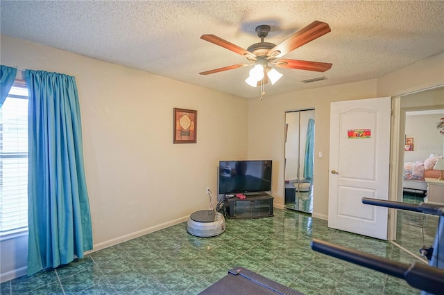 exercise area with ceiling fan and a textured ceiling