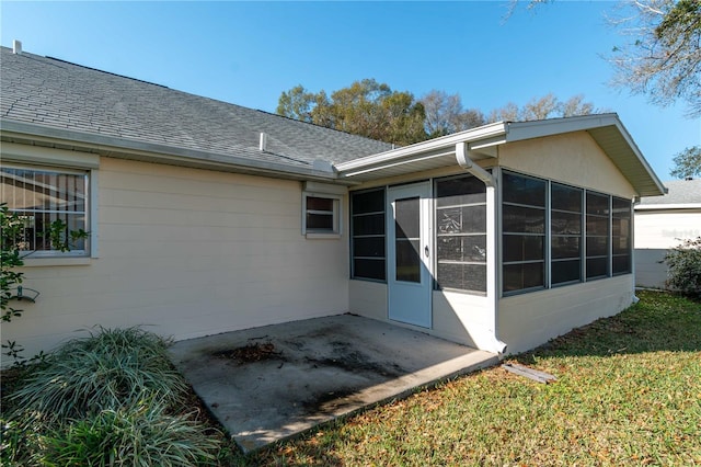 rear view of property featuring a yard, a sunroom, roof with shingles, and a patio