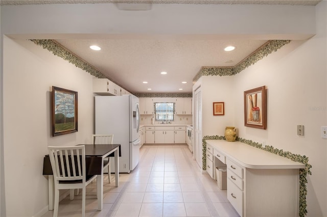 kitchen with light tile patterned floors, light countertops, freestanding refrigerator, white cabinetry, and a textured ceiling