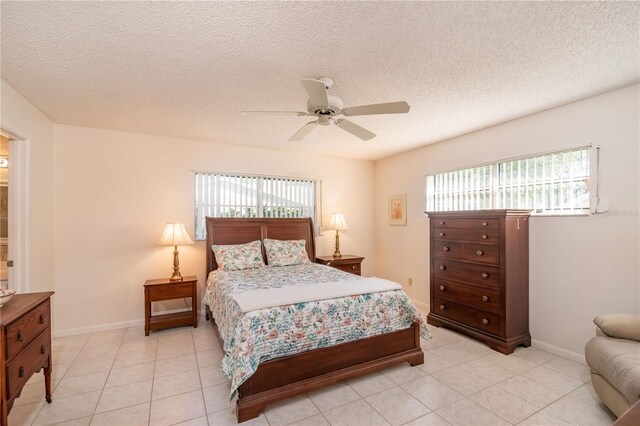 bedroom with a textured ceiling, multiple windows, light tile patterned floors, and a ceiling fan