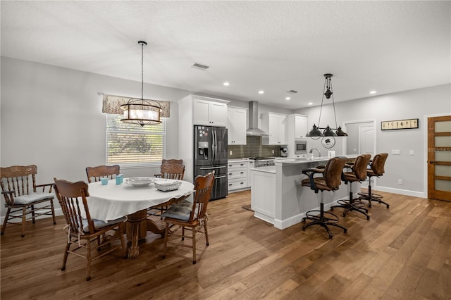 kitchen with wall chimney range hood, white cabinetry, refrigerator with ice dispenser, and pendant lighting