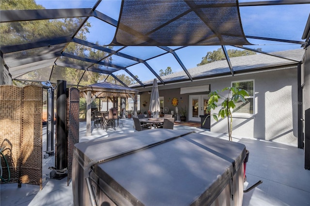 view of patio featuring glass enclosure, a gazebo, a hot tub, and french doors