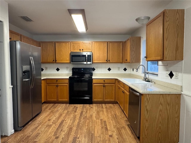 kitchen with tasteful backsplash, appliances with stainless steel finishes, sink, and light hardwood / wood-style flooring