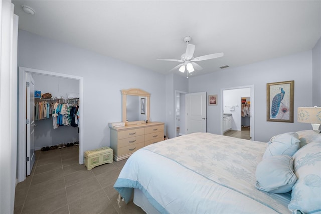 tiled bedroom featuring ensuite bathroom, a closet, ceiling fan, and a walk in closet