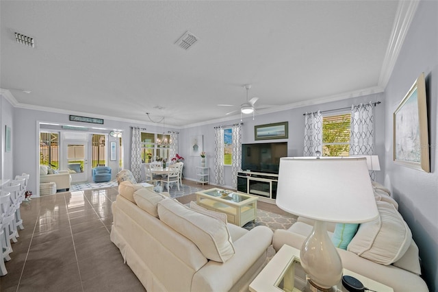 tiled living room with ceiling fan with notable chandelier and crown molding