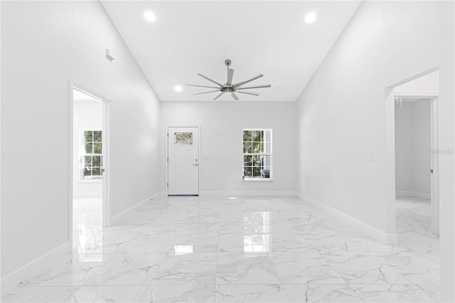 empty room featuring ceiling fan, a towering ceiling, and a healthy amount of sunlight