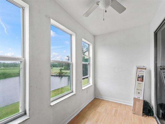 unfurnished sunroom featuring ceiling fan, a water view, and a wealth of natural light