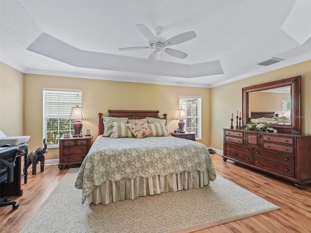 bedroom with crown molding, ceiling fan, a raised ceiling, and light hardwood / wood-style floors