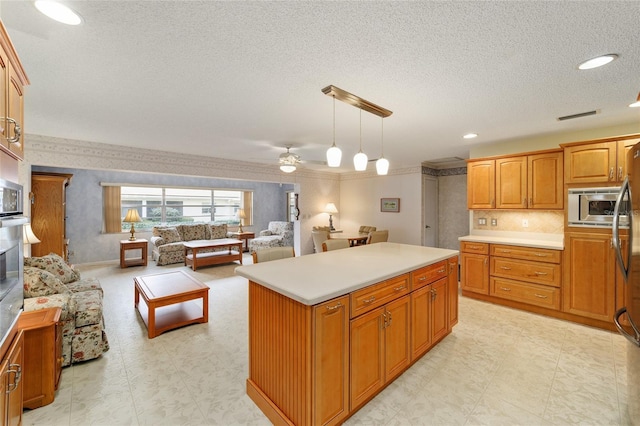 kitchen featuring stainless steel microwave, a textured ceiling, decorative light fixtures, a kitchen island, and ceiling fan