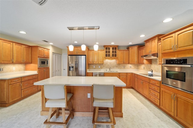 kitchen featuring a kitchen island, stainless steel appliances, decorative backsplash, a kitchen breakfast bar, and sink