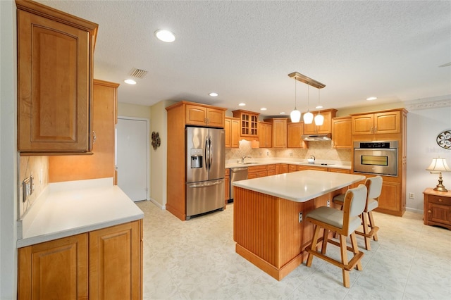 kitchen featuring pendant lighting, a kitchen island, stainless steel appliances, decorative backsplash, and a breakfast bar area