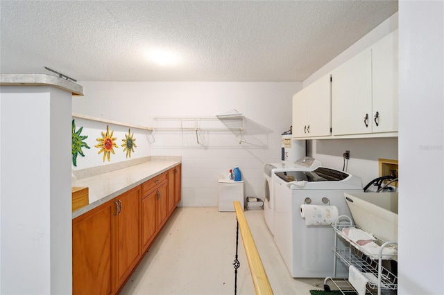 laundry room featuring washing machine and dryer, a textured ceiling, and cabinets