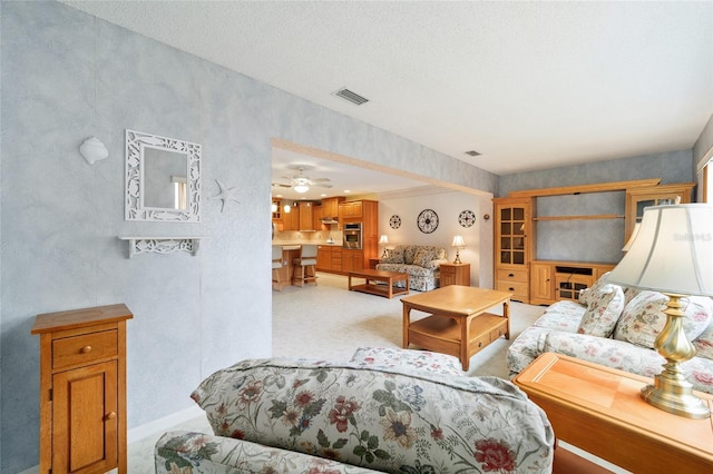 living room featuring light carpet, a textured ceiling, and ceiling fan