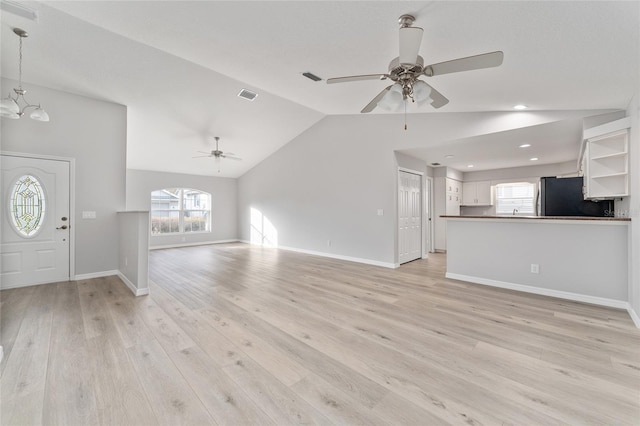 unfurnished living room featuring ceiling fan with notable chandelier, lofted ceiling, and light wood-type flooring