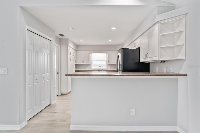 kitchen with kitchen peninsula, light hardwood / wood-style flooring, stainless steel fridge, sink, and white cabinets