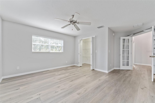 spare room with light wood-type flooring, ceiling fan, french doors, and a textured ceiling