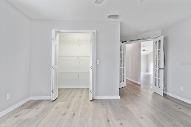 unfurnished bedroom with light hardwood / wood-style flooring, french doors, a textured ceiling, a walk in closet, and a closet