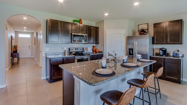 kitchen featuring appliances with stainless steel finishes, sink, a kitchen bar, a kitchen island with sink, and stone counters