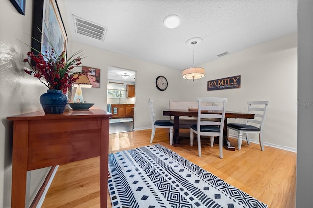 dining area featuring light wood-style floors, visible vents, a textured ceiling, and baseboards