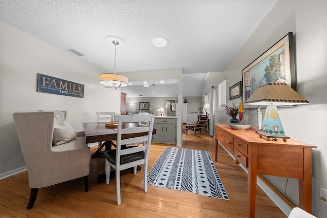 dining space with light wood finished floors, baseboards, visible vents, and a textured ceiling