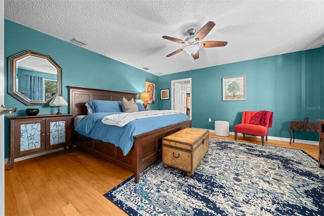 bedroom featuring baseboards, visible vents, ceiling fan, wood finished floors, and a textured ceiling