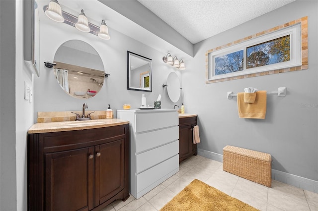 full bath with a sink, a textured ceiling, baseboards, and two vanities