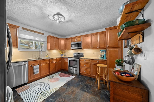 kitchen with light stone counters, stainless steel appliances, a sink, decorative backsplash, and brown cabinetry