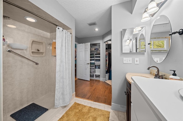 bathroom with visible vents, tiled shower, tile patterned flooring, a textured ceiling, and vanity