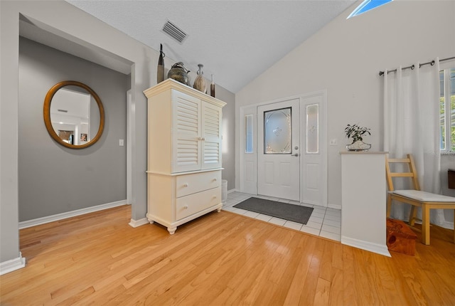 foyer entrance with light wood finished floors, lofted ceiling, visible vents, a textured ceiling, and baseboards