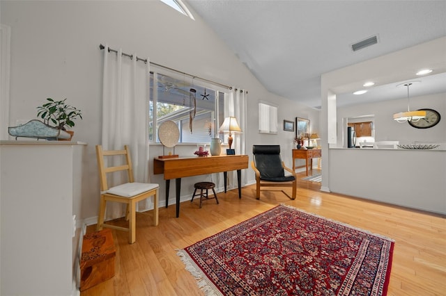 living area with lofted ceiling, visible vents, baseboards, and wood finished floors