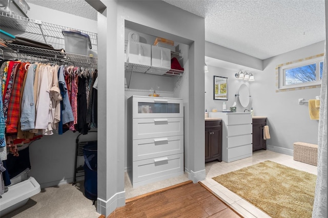 bathroom featuring baseboards, wood finished floors, a spacious closet, a textured ceiling, and vanity