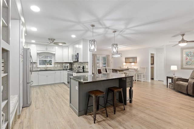 kitchen featuring appliances with stainless steel finishes, a kitchen island, white cabinetry, hanging light fixtures, and a breakfast bar