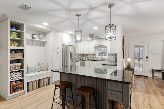 kitchen with stainless steel refrigerator, decorative light fixtures, dark stone countertops, white cabinets, and light hardwood / wood-style floors