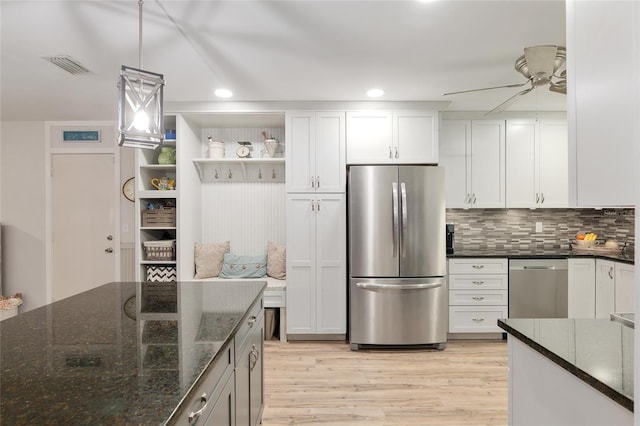 kitchen with pendant lighting, white cabinets, stainless steel appliances, dark stone counters, and light hardwood / wood-style floors