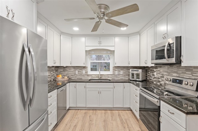 kitchen with sink, white cabinetry, light hardwood / wood-style flooring, dark stone counters, and stainless steel appliances