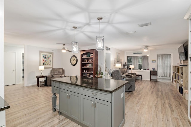 kitchen featuring hanging light fixtures, light wood-type flooring, dark stone countertops, a kitchen island, and gray cabinets