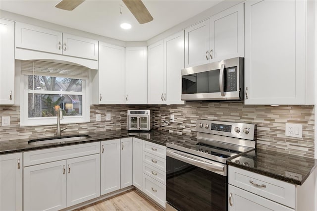 kitchen with white cabinetry, sink, stainless steel appliances, and dark stone countertops