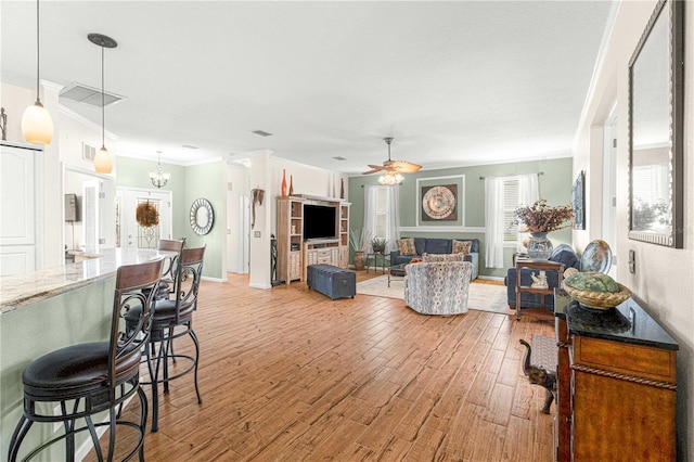 living room featuring ornamental molding, ceiling fan with notable chandelier, and light hardwood / wood-style flooring