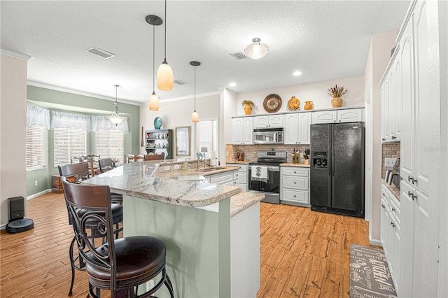 kitchen with appliances with stainless steel finishes, pendant lighting, white cabinets, a kitchen bar, and ornamental molding