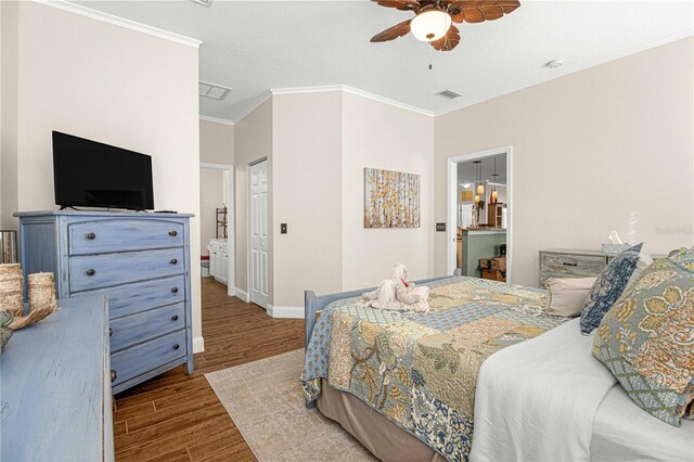 bedroom with crown molding, ceiling fan, wood-type flooring, and ensuite bath