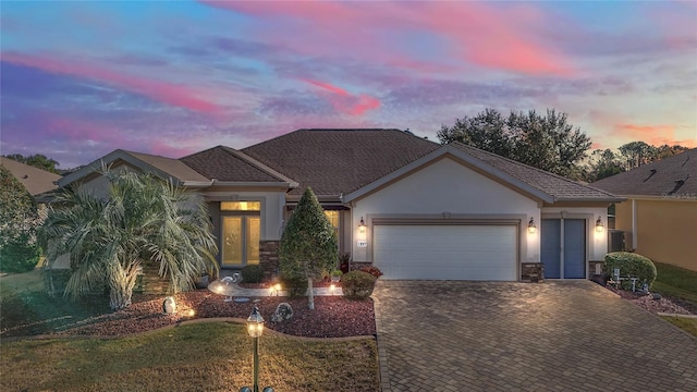 view of front of house with stone siding, decorative driveway, an attached garage, and stucco siding