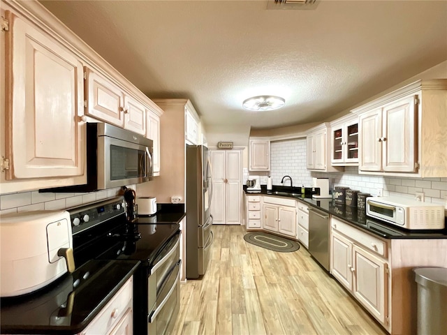 kitchen featuring sink, light wood-type flooring, a textured ceiling, stainless steel appliances, and tasteful backsplash