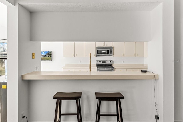 kitchen featuring stainless steel appliances, a textured ceiling, a kitchen bar, and kitchen peninsula