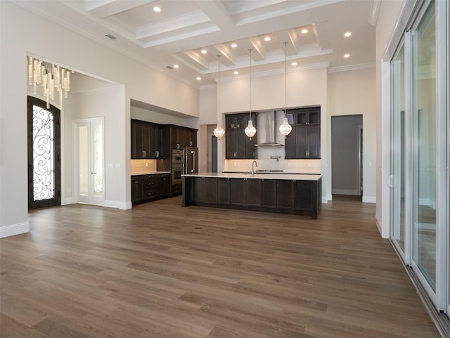 kitchen featuring tasteful backsplash, a towering ceiling, wall chimney exhaust hood, and an island with sink