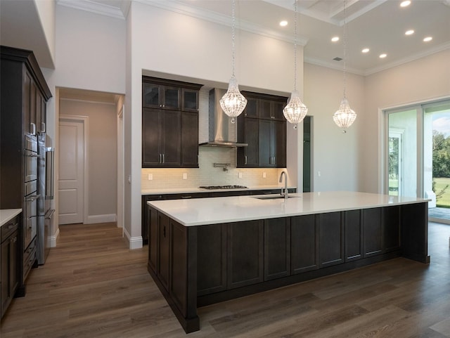 kitchen with pendant lighting, sink, a kitchen island with sink, dark brown cabinets, and wall chimney exhaust hood