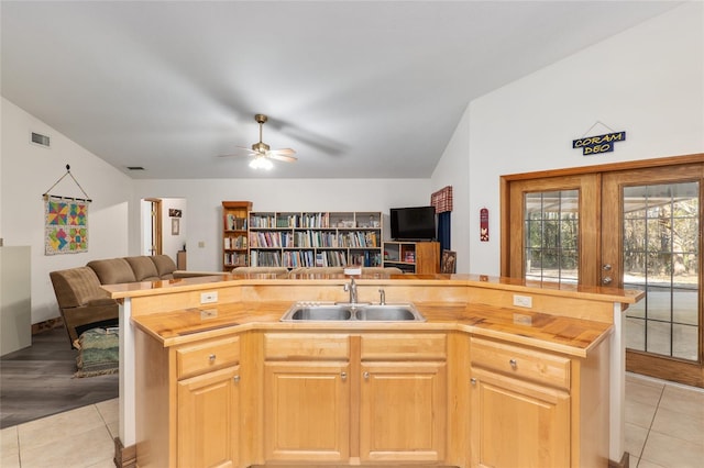 kitchen featuring lofted ceiling, sink, butcher block counters, a kitchen island with sink, and light tile patterned flooring