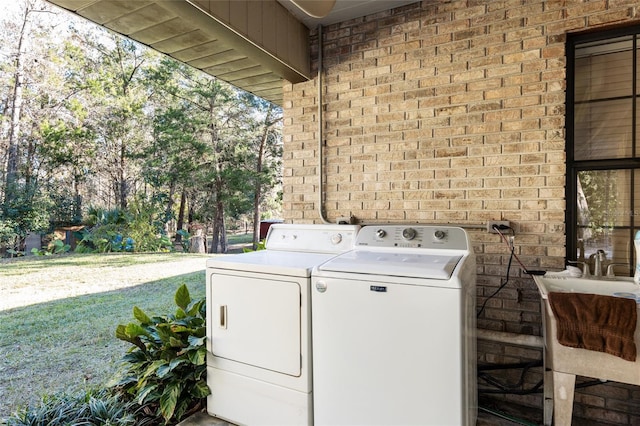 washroom with washing machine and clothes dryer, brick wall, and sink