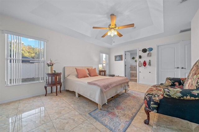 bedroom featuring ceiling fan, ensuite bathroom, and a tray ceiling